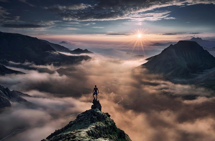 A medio atardecer un hombre parado en la cima de una montaña viendo en dirección a otras montañas 