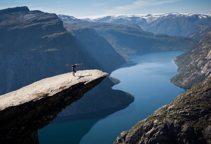 Chica practicando algunos paso de gimnasia a la orilla de una roca entre montañas en Noruega 