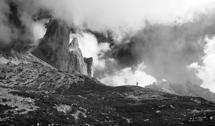 Una persona caminando hacia una montaña con el cidelo un poco nublado 