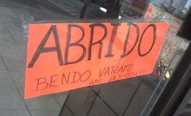 Letrero en color naranja con muchas faltas de ortografía en la puerta de un negocio 