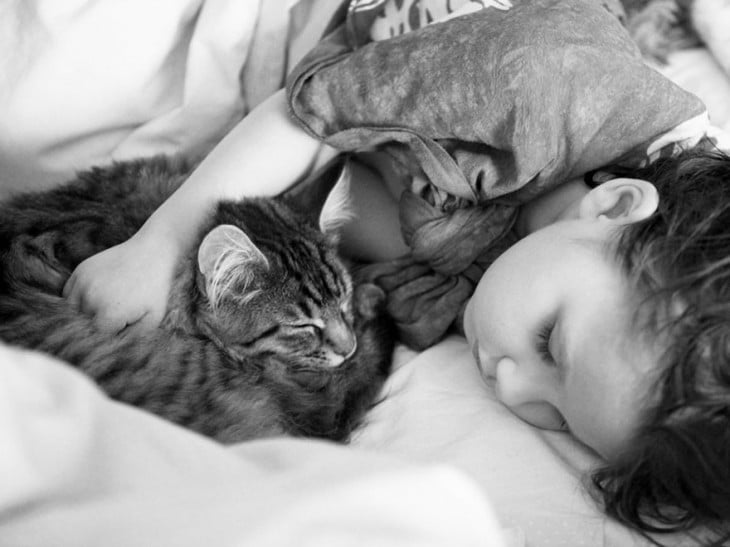 Imagen en blanco y negro de una niña abrazada de su gato mientras duerme 