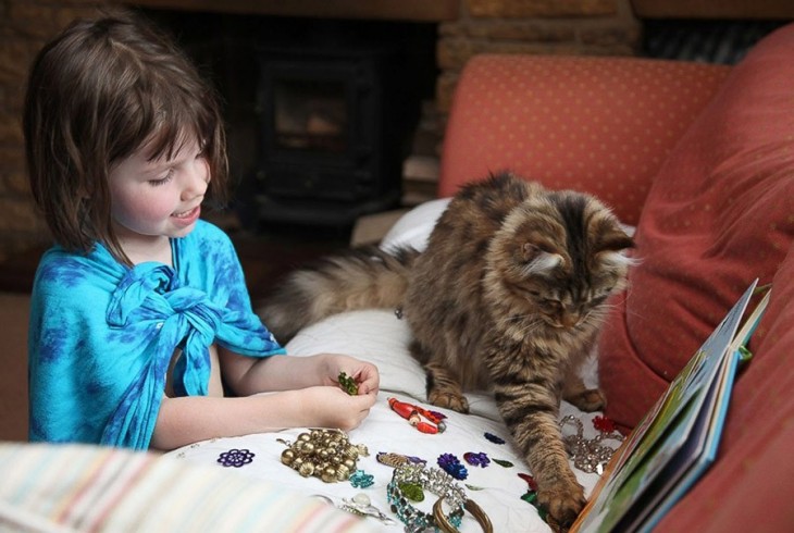 Niña y su gato sobre un sillón con algunos aretes y pulseras en la mano 