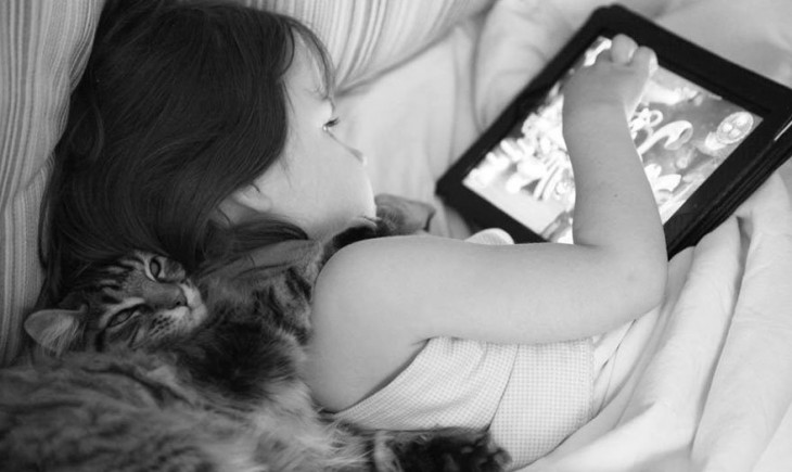 Niña usando un iPad y su gato trás de ella 