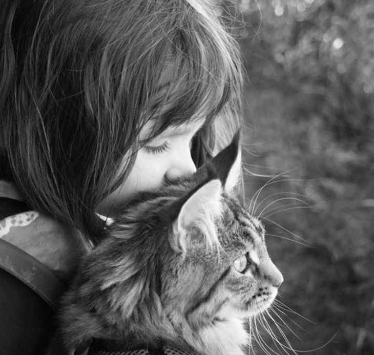 Niña detrás de su gato observando hacia enfrente 