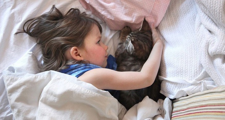 Niña recostada en la cama abrazando a su gato 