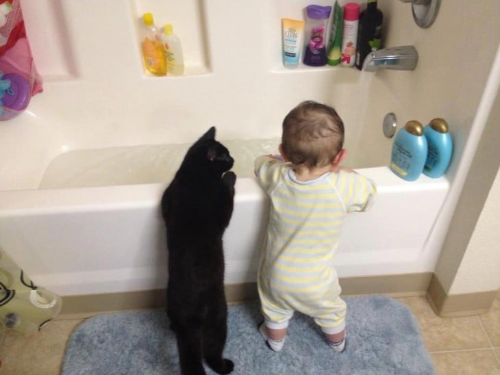Un niño y un gato parados sobre una tina de baño 