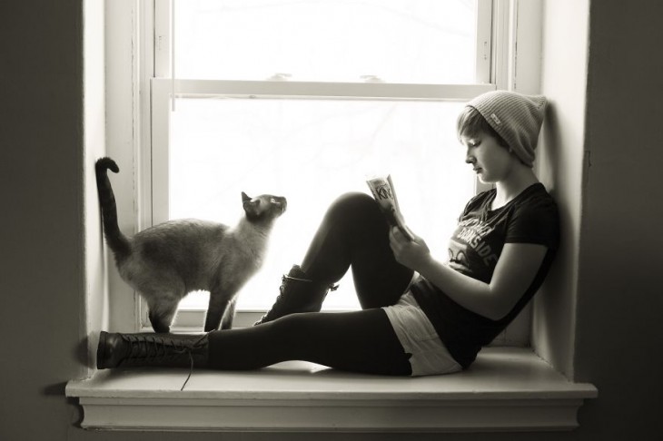 Chica acostada en una ventana y un gato frente a ella 