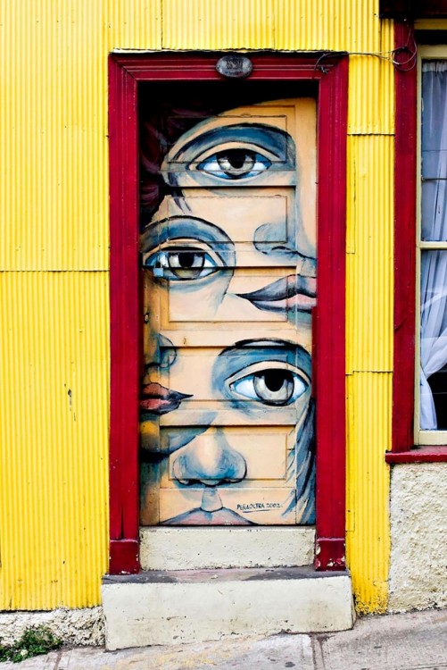 Puerta con un marco de color rojo y diferentes ojos pintados en la puerta 