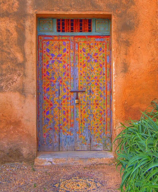 Puerta ubicada en Marruecos con una pequeña ventana en la parte superior y diseños en colores morados y anaranjados en su diseño 