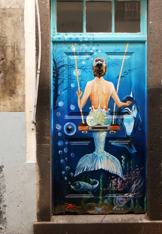 Puerta con un diseño de sirena en un columpio y un delfín frente de ella con algunos peces debajo simulando un mar