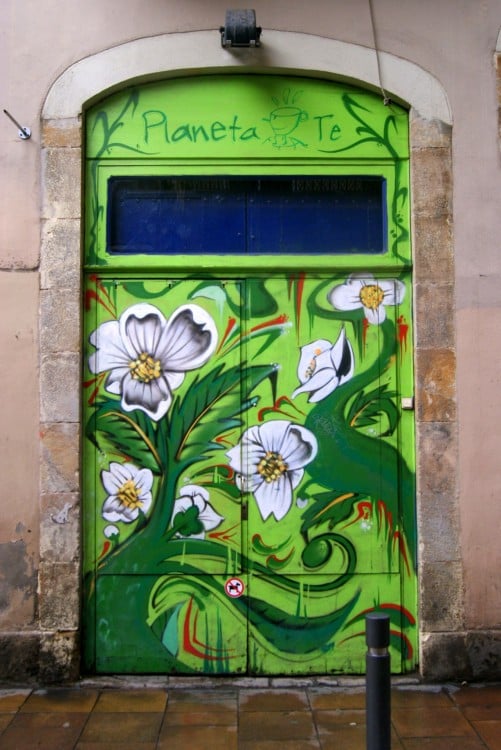 Puerta en color verde con diseños de flores en la mayor parte de su superficie con un letrero en la parte superior que dice "Planeta Té"