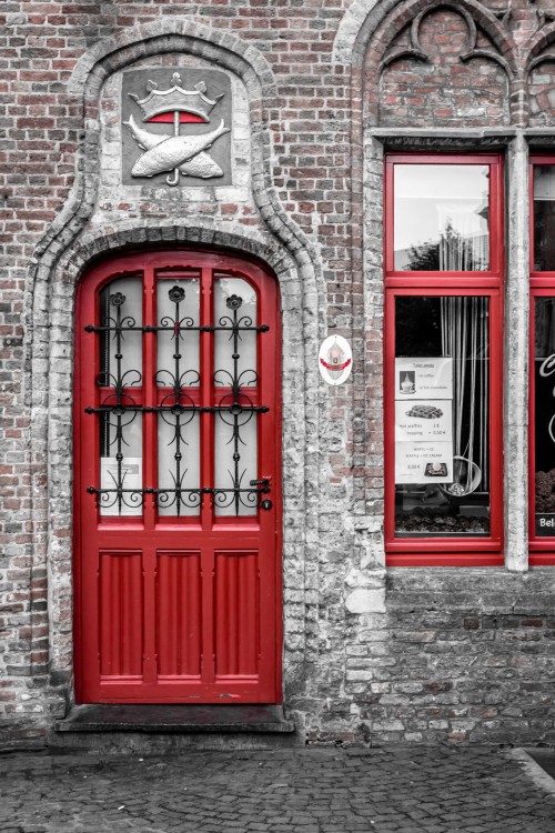 Puerta de color rojo con barandales en color negro que cubren tres filas de vidrios en la parte superior de la puerta 