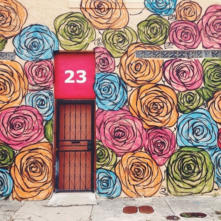 Casa con decoración de rosas alrededor de una puerta con barandal negro y un número 23 en un fondo rosa 