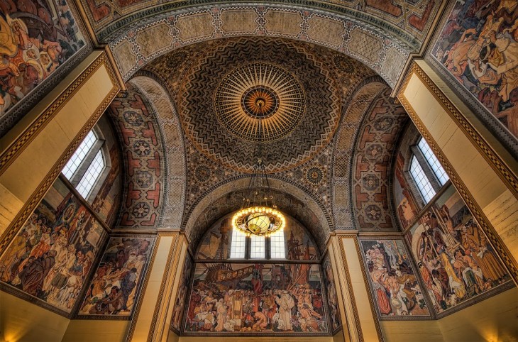 Biblioteca con diseños de personas romanas en sus paredes, arcos y su techo con circulo de figuras en colores opacos 