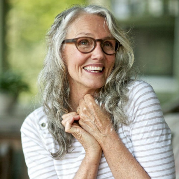 Mujer de la tercera edad sonriendo y con las manos dobladas hacia su pecho 