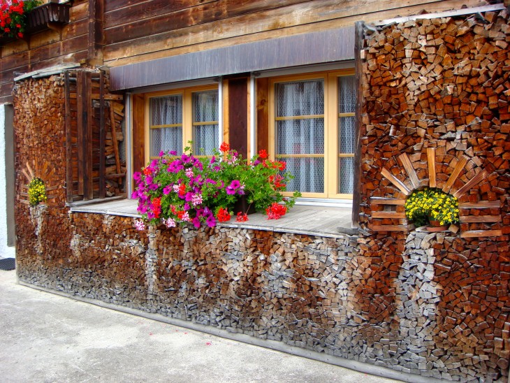 Pedazos de madera apilados de forma que rodean las ventanas de una casa con distintos colores 