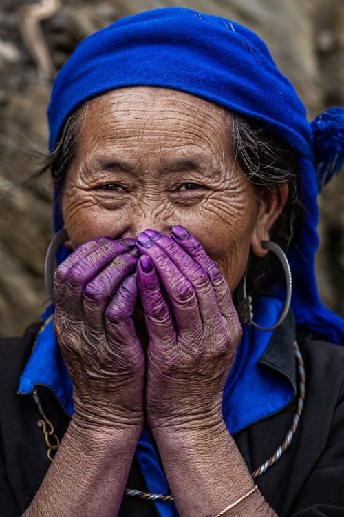 mujer con un reboso en la cabeza color azul y las manos en la boca pintadas de color purpura 
