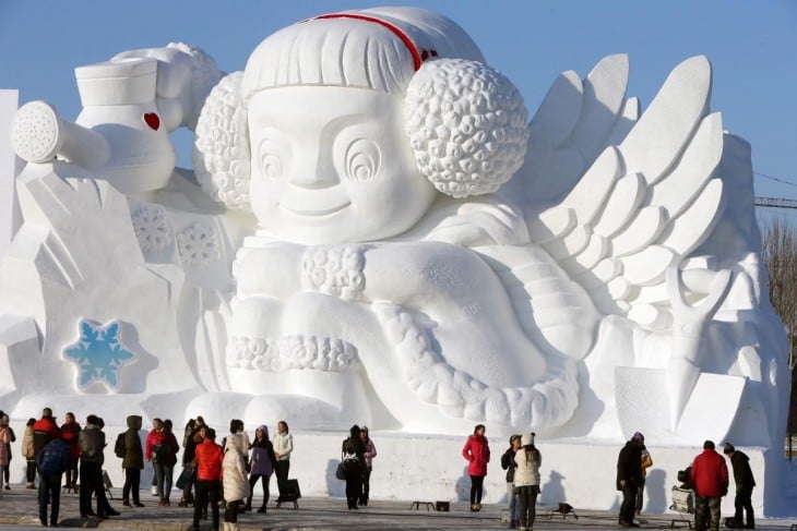 escultura de un niño sentado hecha con nieve y siendo observada por personas