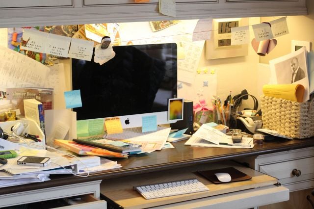 escritorio con una computadora lleno de papeles y notas pegadas en la pared 