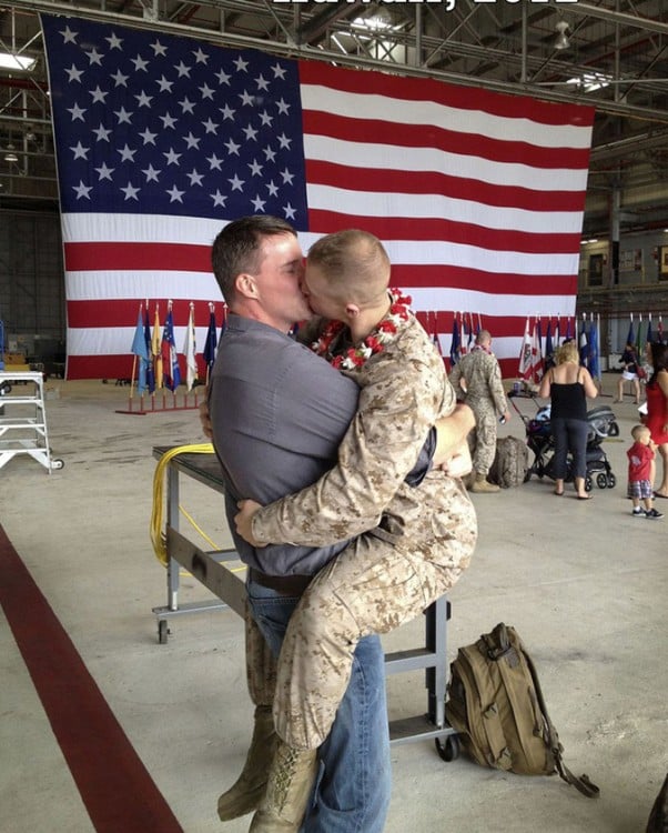 soldado besando a su novio con la bandera de estados unidos tras ellos 