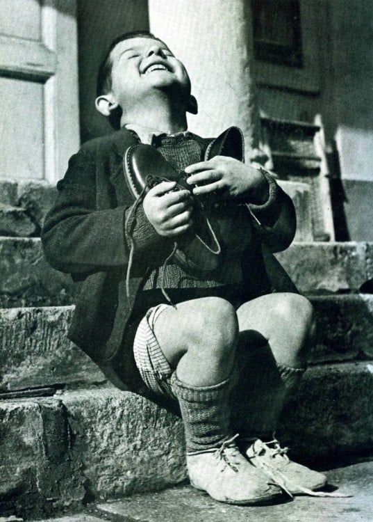 niño sosteniendo un par de zapatos en su pecho mientras se muestra emocionado y ríe