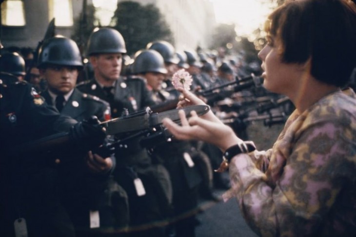 joven coloca una flor sobre los rifles de policías durante la guerra 