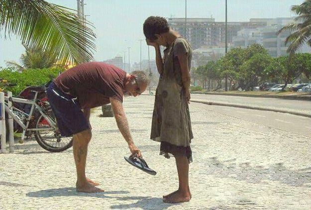 hombre entrega sus sandalias a una mujer indigente que esta en la acera