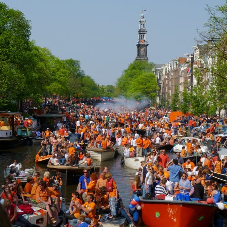 personas vestidas de naranja en unas canoas que van por un canal de agua 