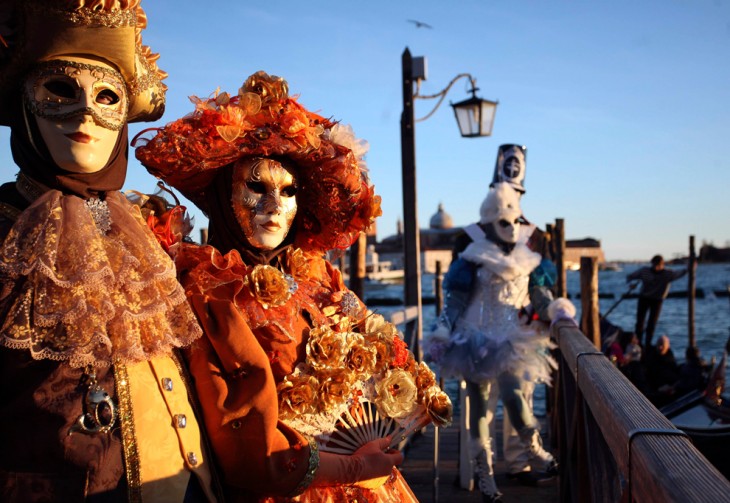 personas con atuendos extravagantes usando mascaras y caminando por las calles de Venecia 