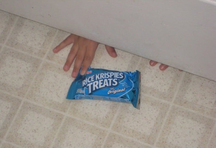 niño tomando un paquete de galletas abajo de la puerta 