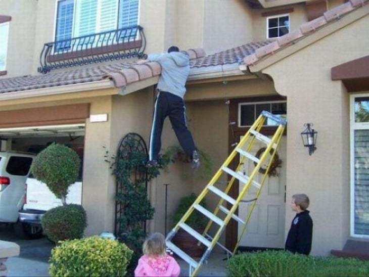 persona colgada del techo de una casa con una escalera a un lado y niños que lo están observando 