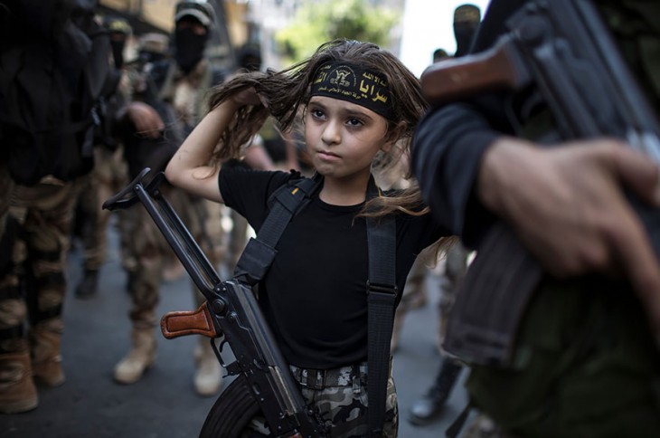 niña con un rifle colgando sobre su pecho mientras ella se toca el cabello 