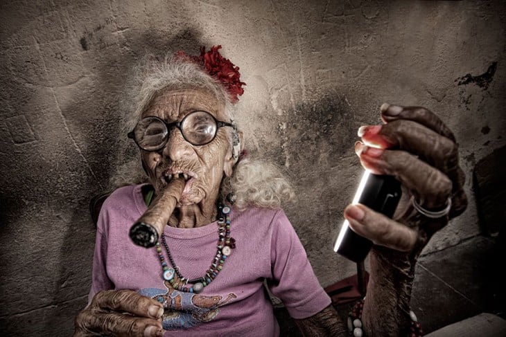 mujer anciana vestida de rosa fumando un puro mientras es fotografiada 
