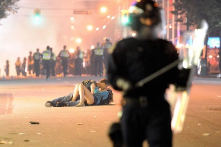 pareja de novios recostados en la acera besándose mientras hay una guerra frente a ellos 