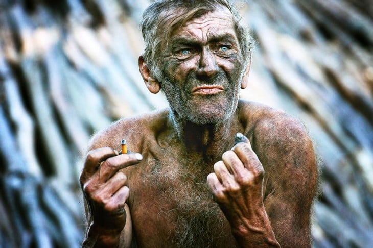 hombre lleno de carbon en el cuerpo y sosteniendo un cigarrillo en su mano 