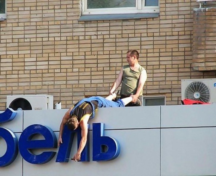 hombre deteniendo al otro de los pies para que arreglen las letras