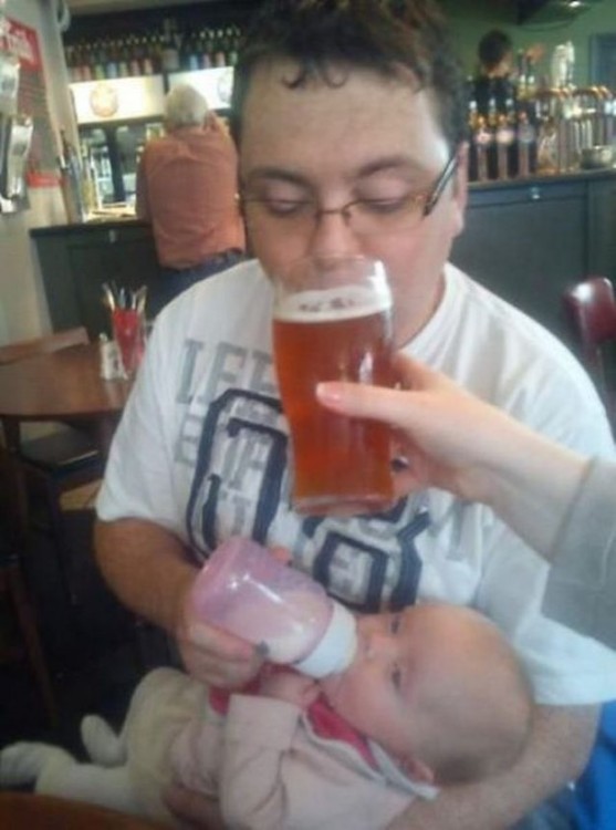amigos le dan cerveza a papa primerizo mientras le da de comer a la bebe
