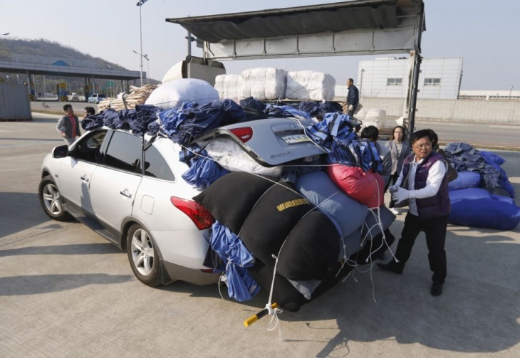 coreano amarrando pacas de ropa en su carro tipo sedan pero ya esta muy lleno