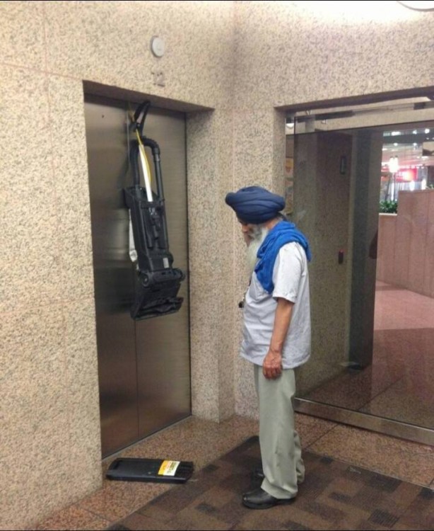 hombre de medio oriente con turbante azul viendo su aspiradora como sedestroza por dejar el cable adentro del ascensor antes de que cerrara