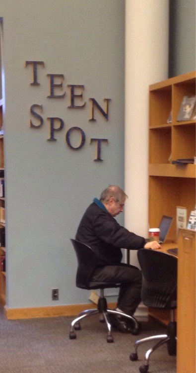 hombre mayor en el area de adolescentes en la biblioteca sentado con su computadora