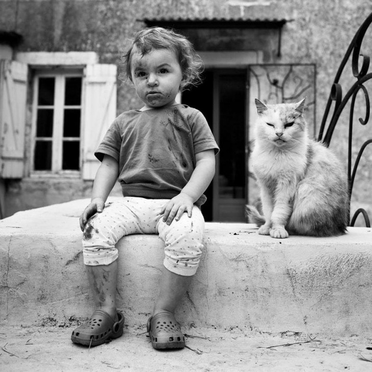 Niño lleno de lodo a un lado de un gato 