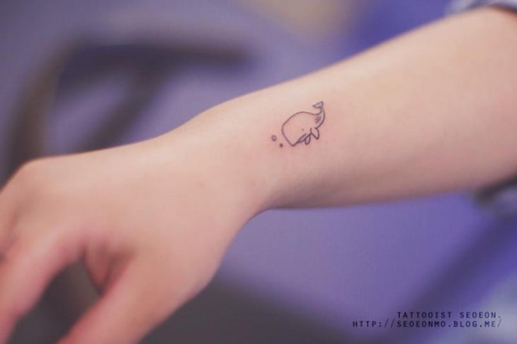 Tatuaje minimalista de ballena en la muñeca de una persona 