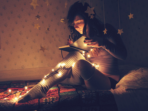 Chica escribiendo en la noche con una serie de luces de navidad 