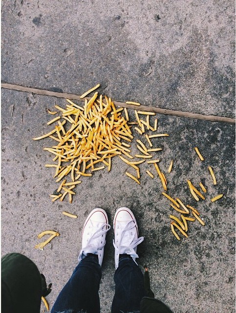 Papas fritas tiradas en el suelo frente a los pies de una persona 