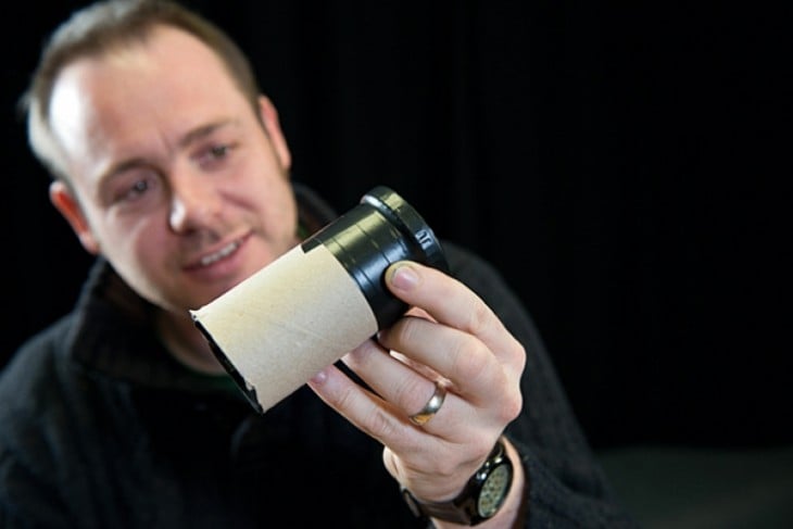 Hombre que tiene un lente fotográfico en su mano con un rollo de papel higiénico 