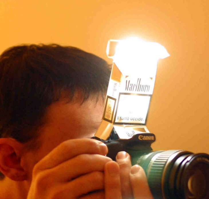 Chico utilizando una cajetilla de cigarros como difusor de luz de un flash para su cámara profesional 