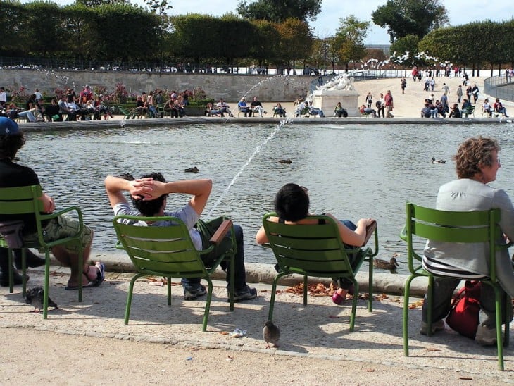 Personas sentadas a la orilla de un lago donde un chico tiene un chorro de agua frente a él 