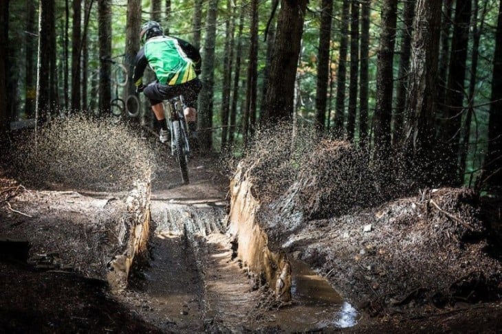 Un hombre en bicicleta pasando un charco donde el agua se derrama por los lados 