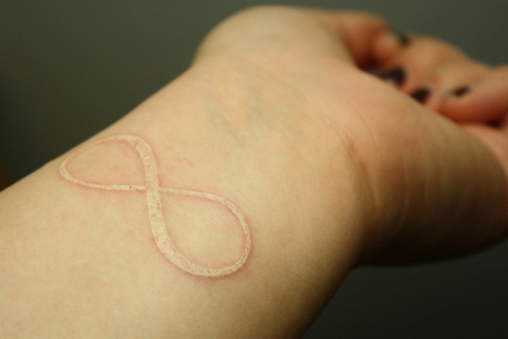 Tatuajes con forma de infinito en tinta blanca sobre el brazo de una chica 