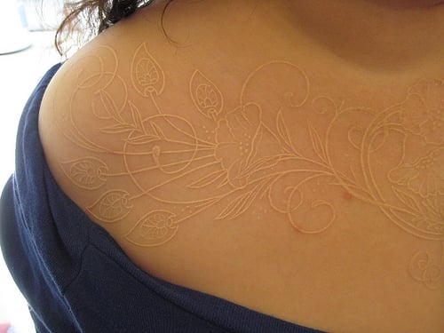 Tatuaje en el pecho de una chica con tinta blanca